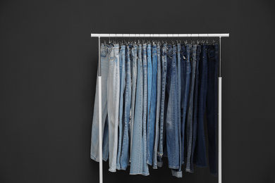 Photo of Rack with different jeans on dark grey background