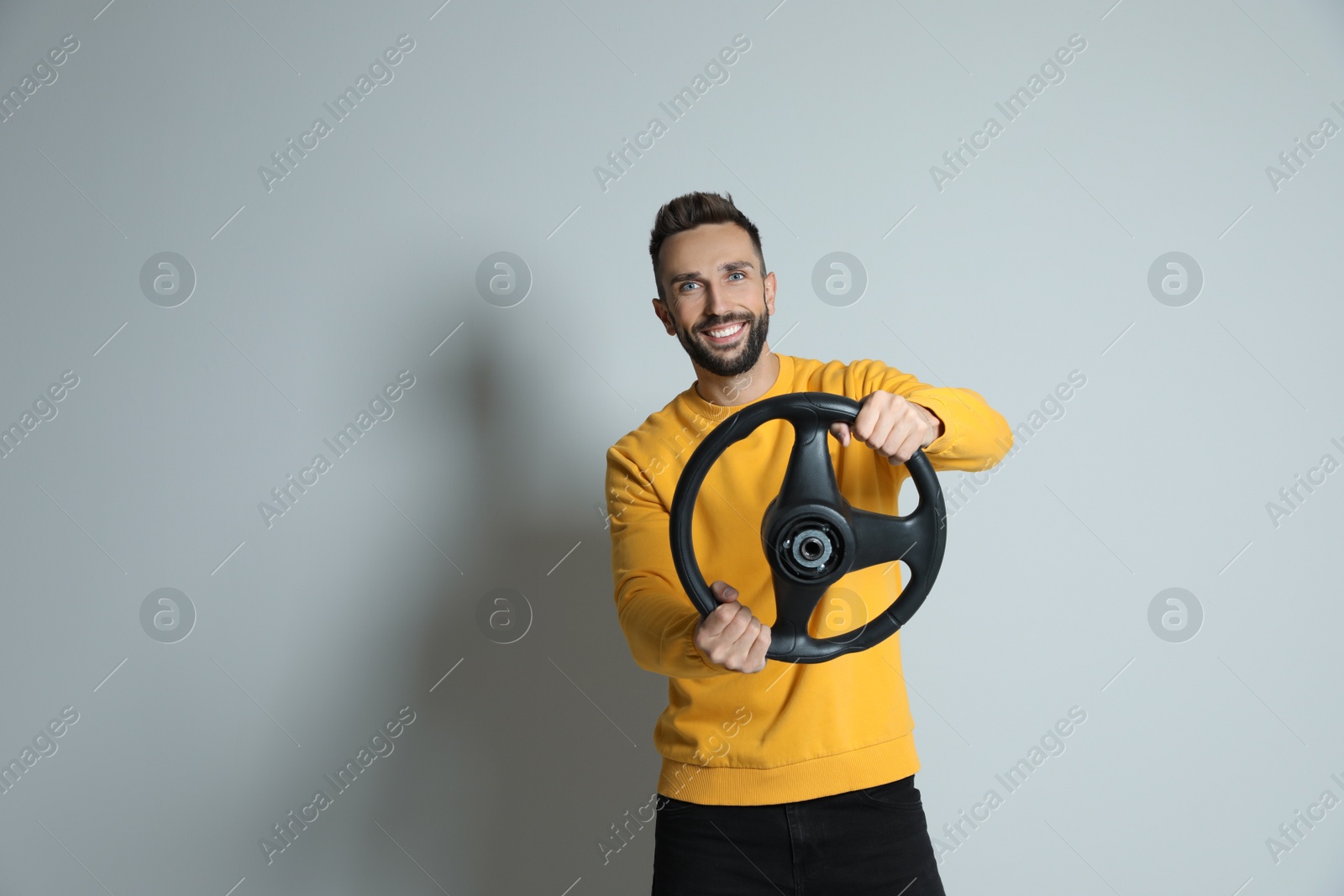 Photo of Happy man with steering wheel on grey background