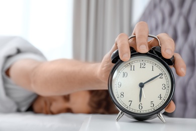 Photo of Sleepy man turning off alarm clock in morning. Bedtime