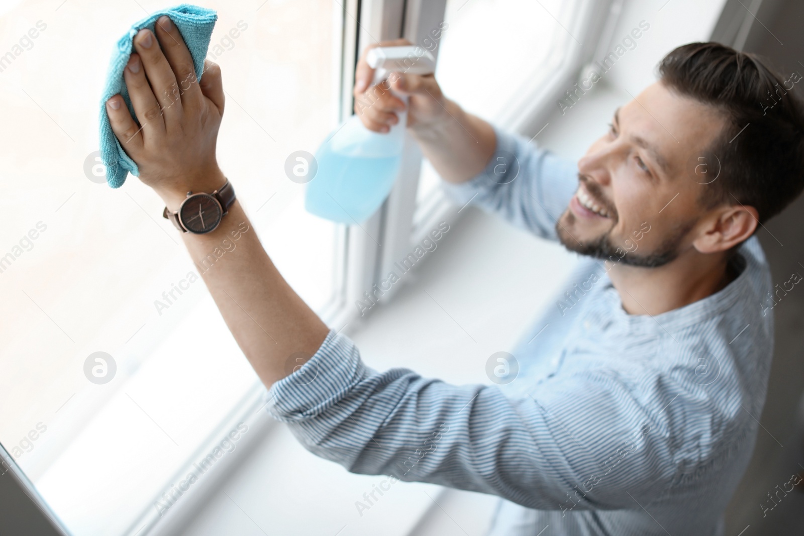 Photo of Man in casual clothes washing window glass at home