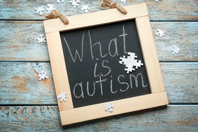 Chalkboard with phrase "What is autism?" and puzzle pieces on wooden background