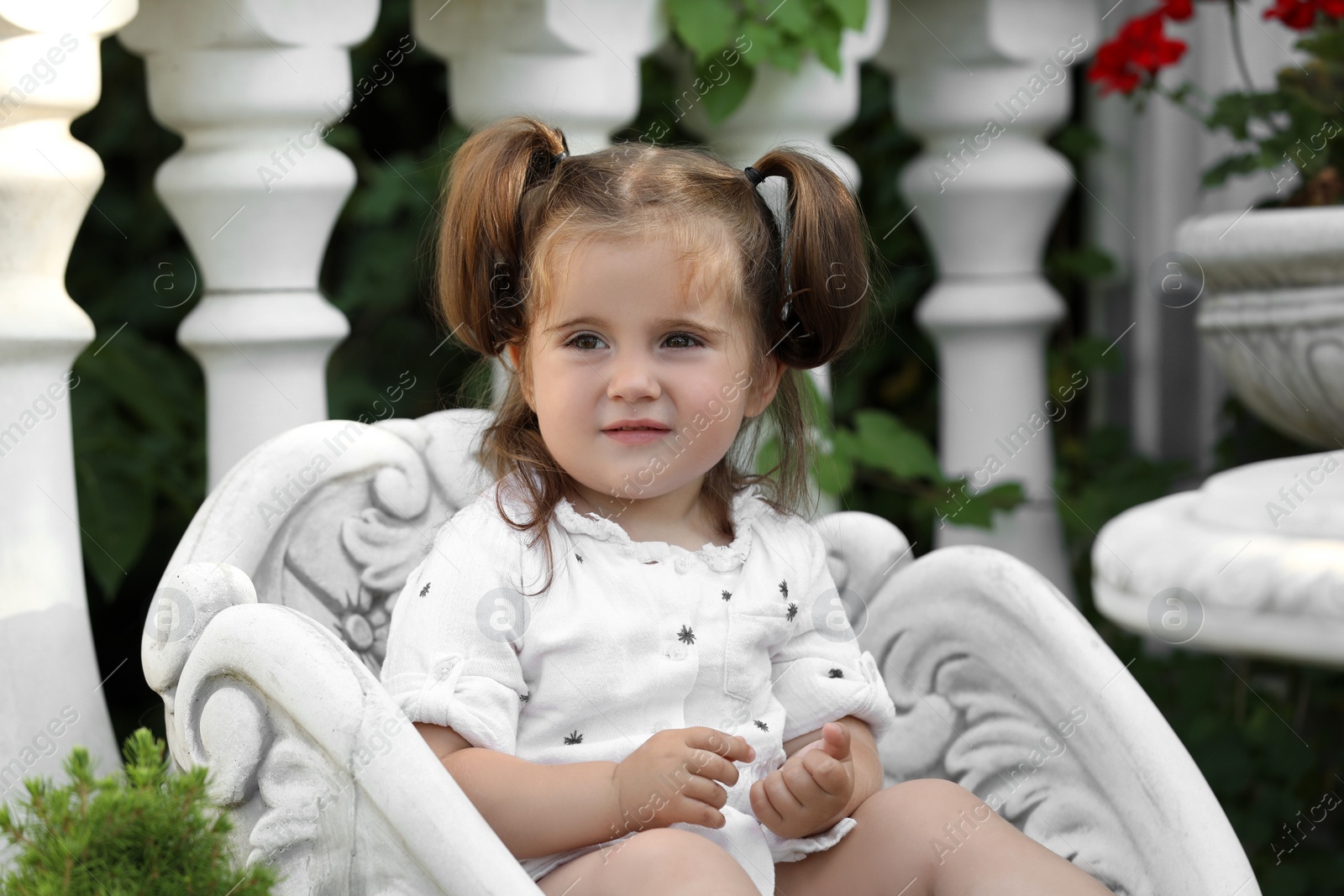 Photo of Cute little girl in white dress sitting in chair outdoors