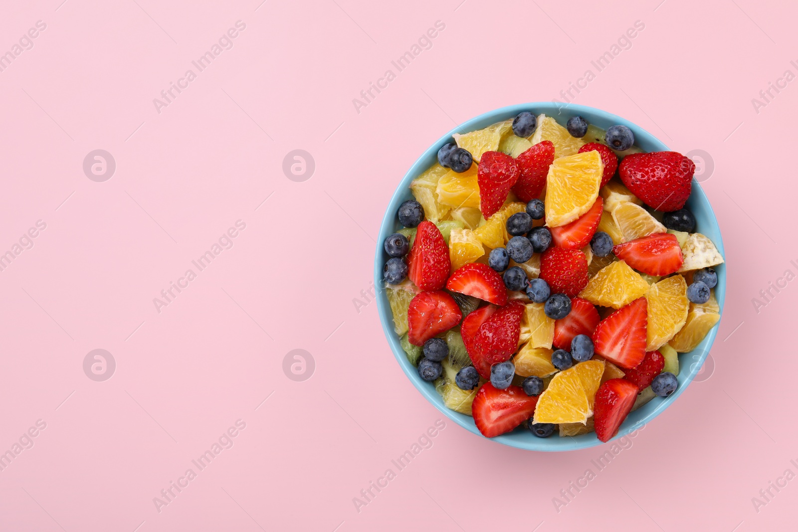 Photo of Yummy fruit salad in bowl on pink background, top view. Space for text