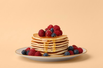 Stack of tasty pancakes with raspberries, blueberries and honey on pale orange background