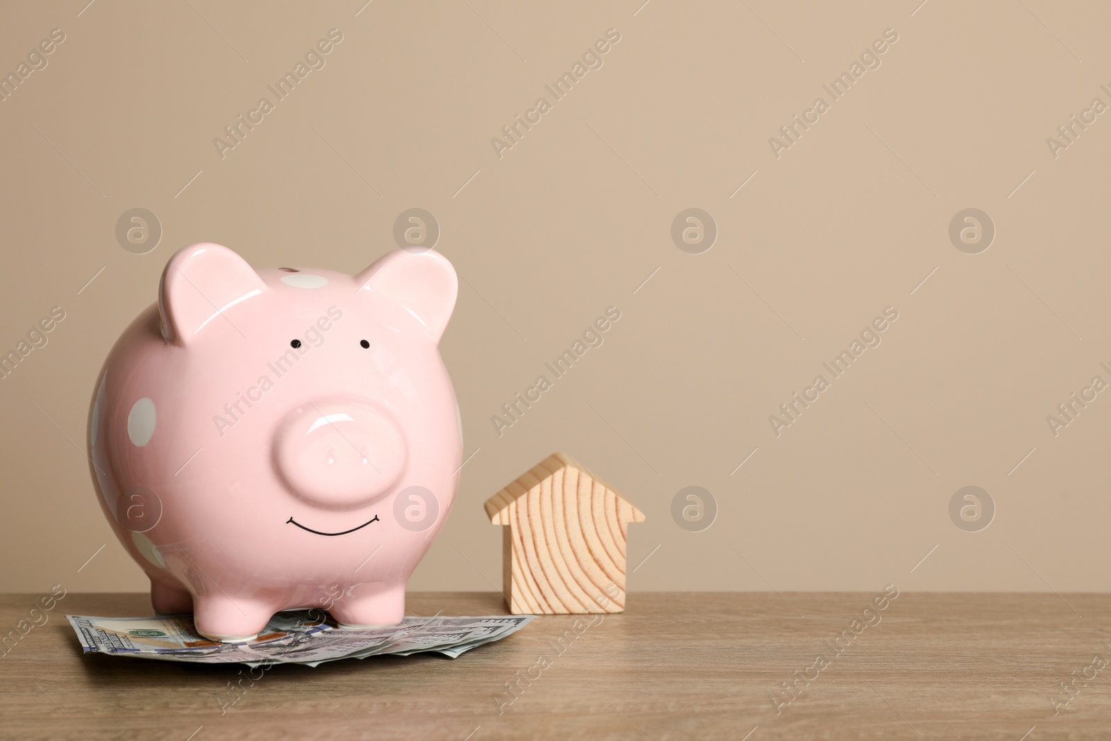 Photo of Piggy bank, dollar banknotes and house model on wooden table against beige background. Space for text