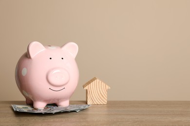 Photo of Piggy bank, dollar banknotes and house model on wooden table against beige background. Space for text