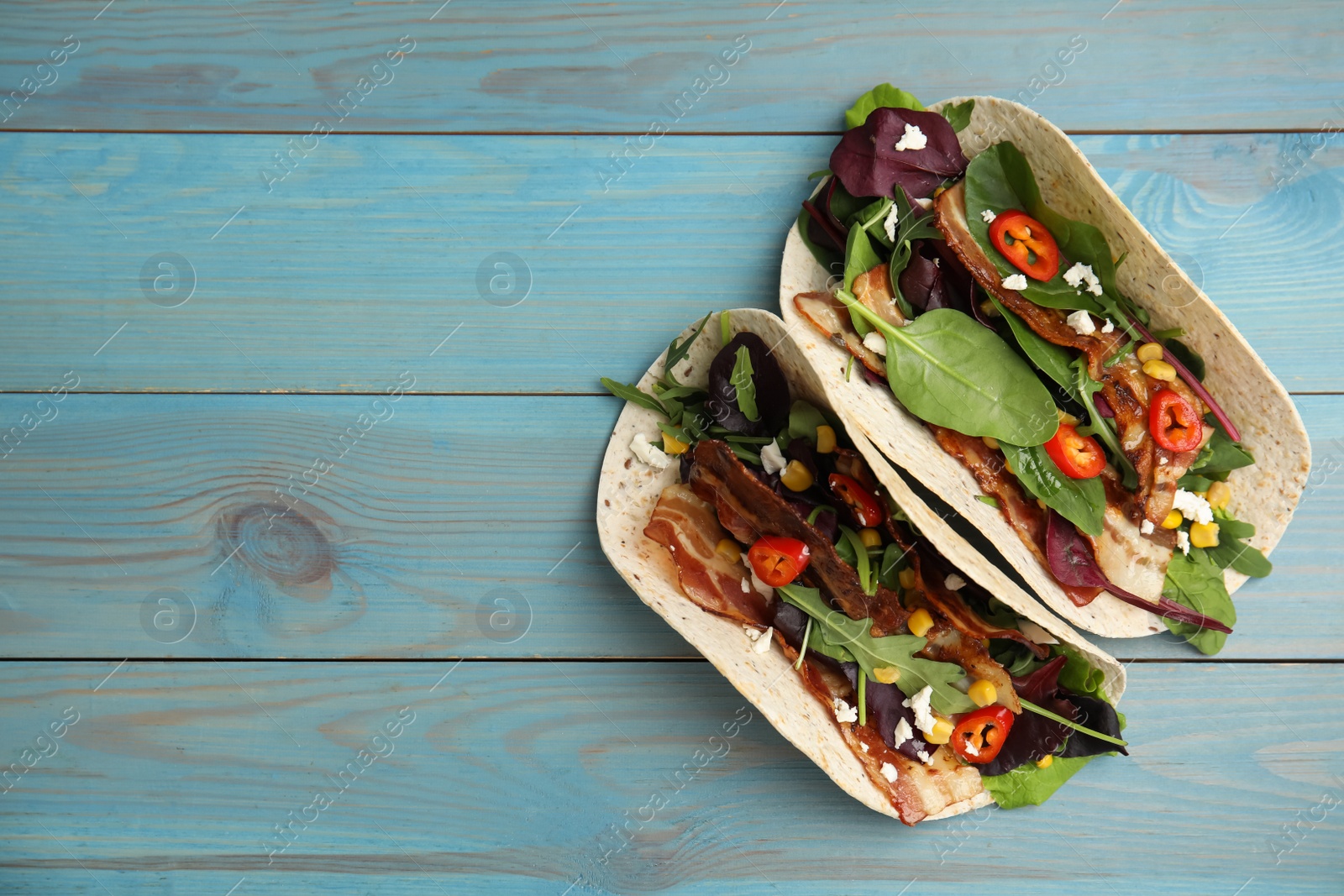 Photo of Delicious tacos with fried bacon, vegetables and cheese on turquoise wooden table, flat lay. Space for text