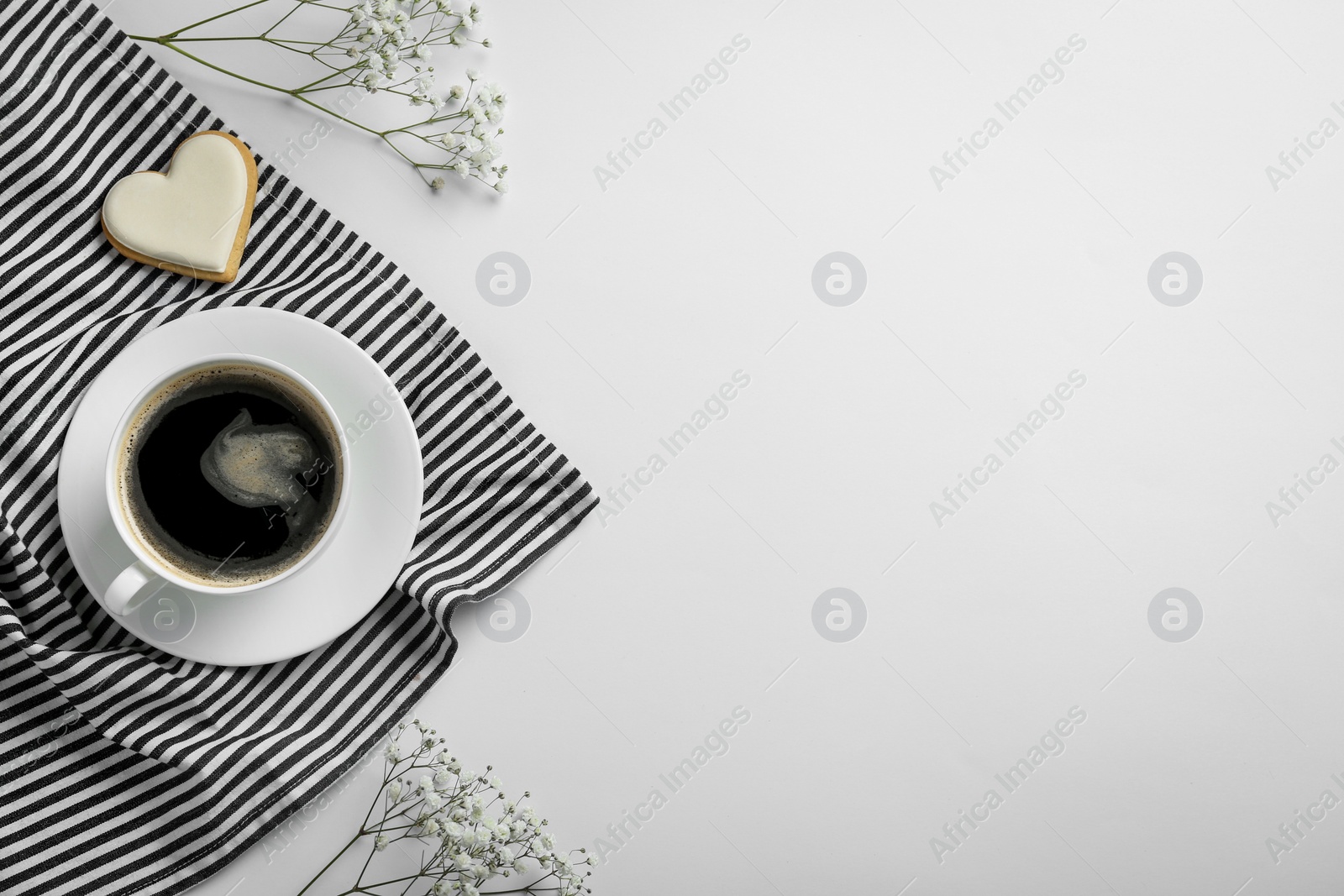 Photo of Cup of coffee, heart shaped cookie, napkin and flowers on white background, top view