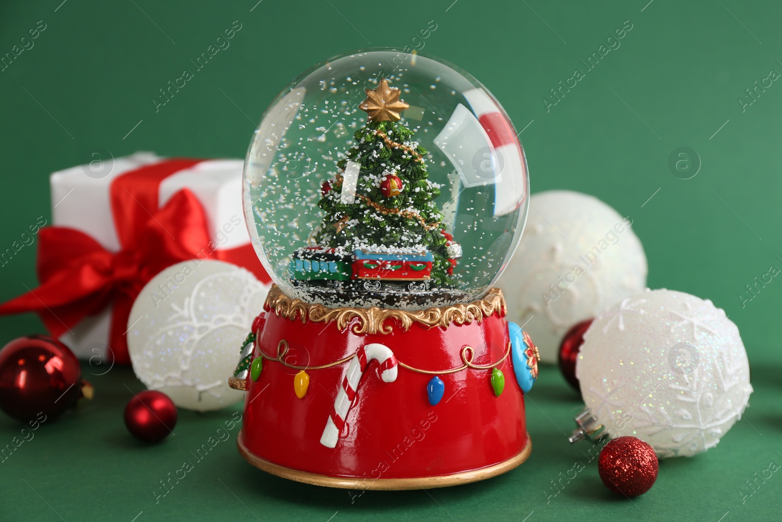 Photo of Beautiful snow globe and Christmas balls on green background