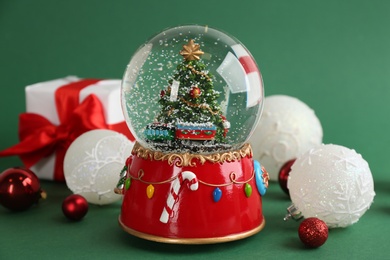 Photo of Beautiful snow globe and Christmas balls on green background