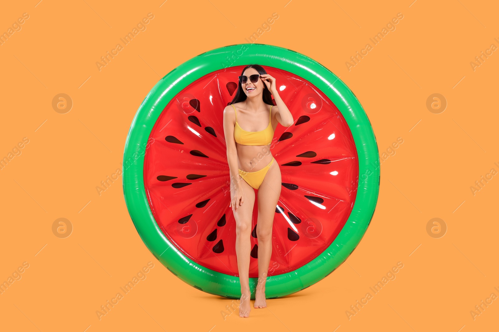 Photo of Happy young woman with beautiful suntan, sunglasses and inflatable mattress against orange background