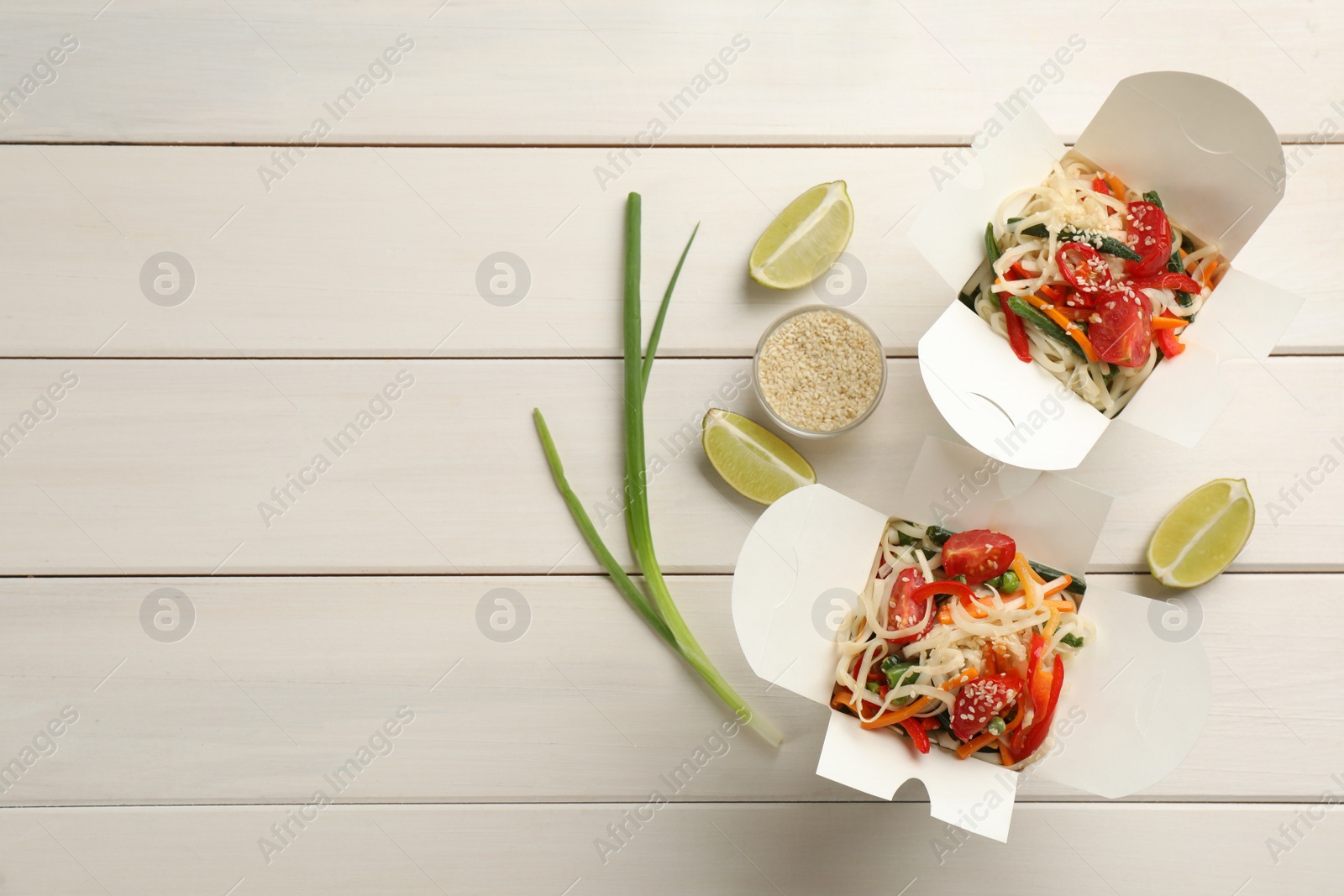 Photo of Boxes of vegetarian wok noodles with ingredients on white wooden table, flat lay. Space for text