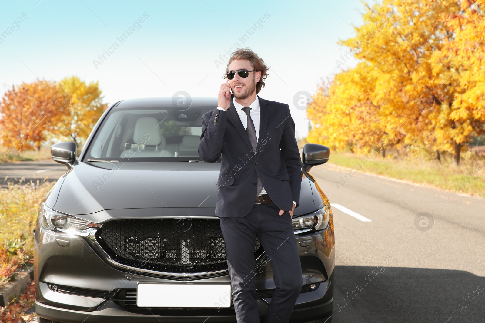 Photo of Young businessman talking on phone near modern car, outdoors