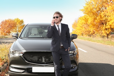 Photo of Young businessman talking on phone near modern car, outdoors