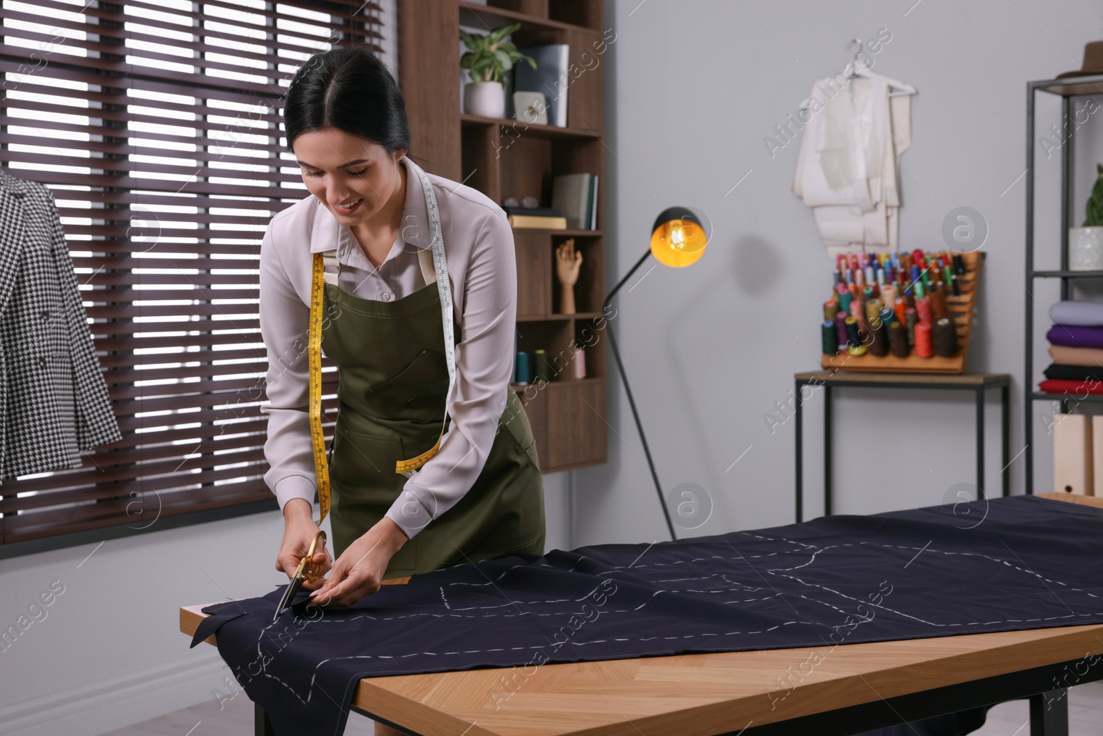 Photo of Dressmaker cutting fabric by following chalked sewing pattern in workshop