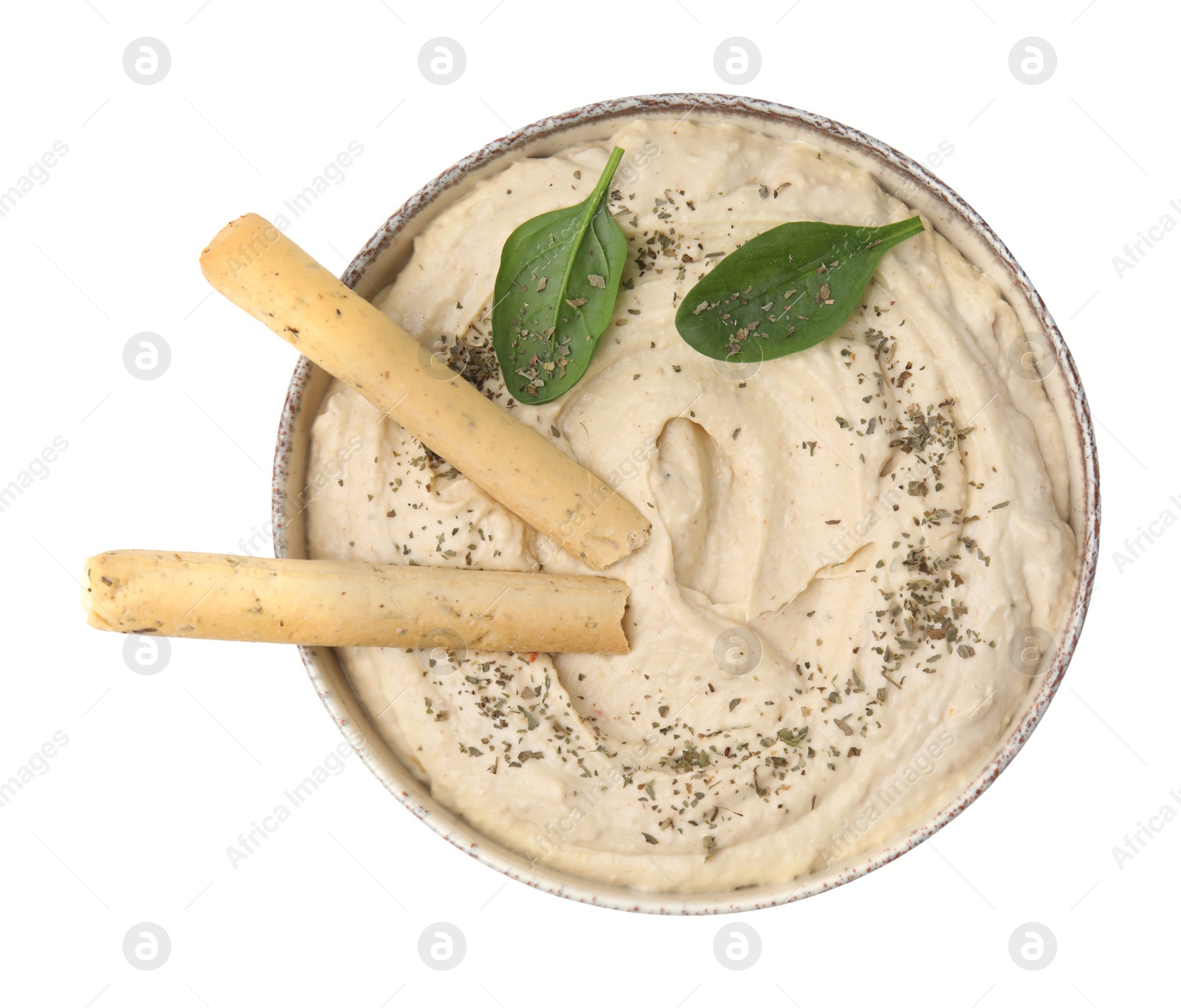 Photo of Bowl of delicious hummus with grissini sticks, basil leaves and spices isolated on white, top view