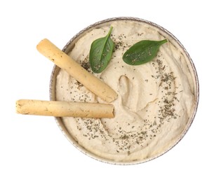 Photo of Bowl of delicious hummus with grissini sticks, basil leaves and spices isolated on white, top view