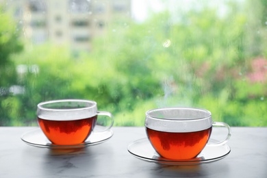 Photo of Cups of hot tea on marble windowsill. Rainy weather