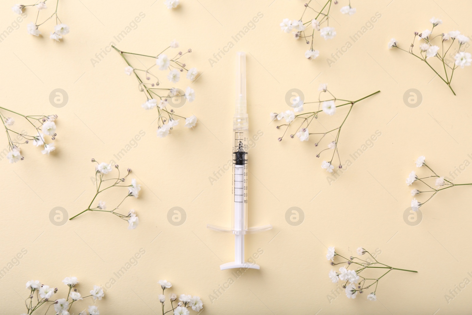 Photo of Cosmetology. Medical syringe and gypsophila flowers on yellow background, flat lay