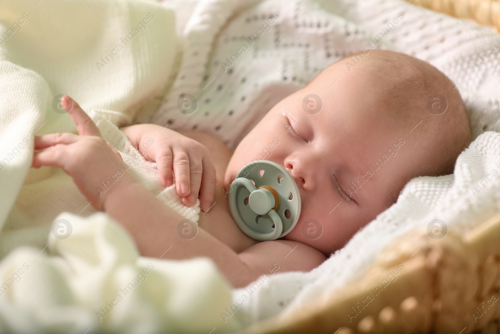 Photo of Cute newborn baby sleeping on white blanket in wicker crib, closeup