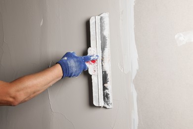 Professional worker plastering wall with putty knife, closeup