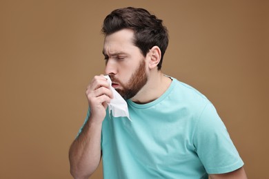Photo of Sick man with tissue coughing on brown background