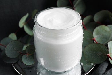 Photo of Jar of hand cream and eucalyptus branches on grey background, closeup