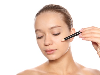 Young woman applying foundation on her face against white background