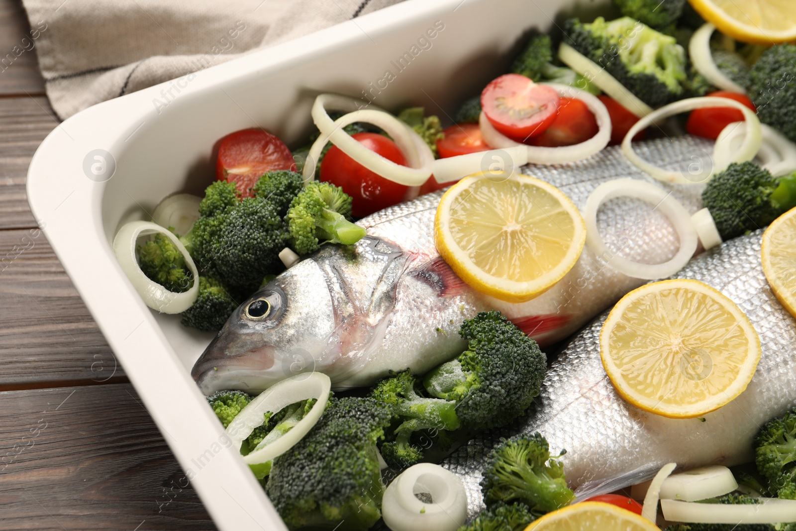 Photo of Raw fish with vegetables and lemon in baking dish on wooden table