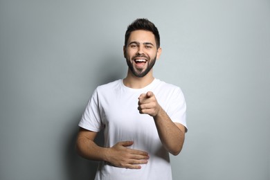 Young man laughing on light grey background. Funny joke