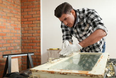 Man repairing old damaged window at table indoors
