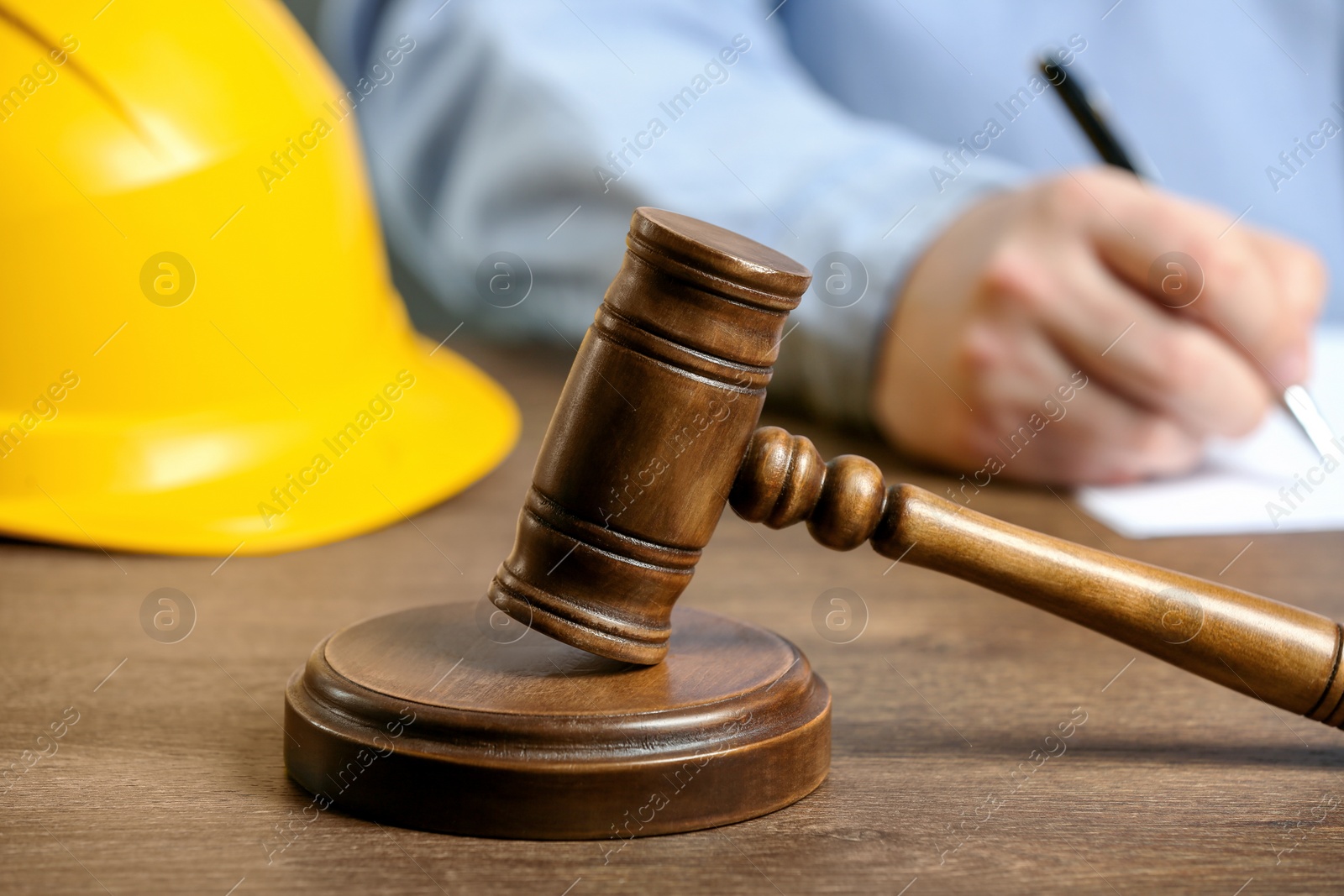 Photo of Construction and land law concepts. Man writing at wooden table, focus on gavel