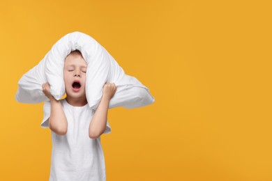 Photo of Sleepy boy with pillow yawning on orange background, space for text. Insomnia problem