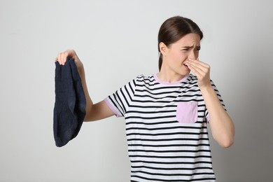 Young woman feeling bad smell from dirty socks on light grey background