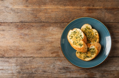 Slices of toasted bread with garlic, cheese and herbs on wooden table, top view. Space for text