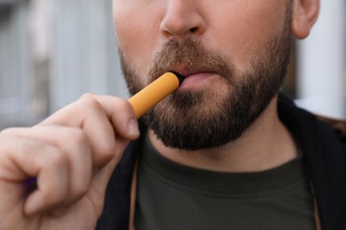 Photo of Handsome young man using disposable electronic cigarette outdoors, closeup