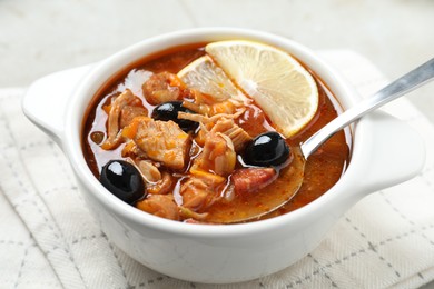 Photo of Meat solyanka soup with sausages, olives, vegetables and spoon in bowl on white table, closeup