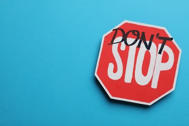 Photo of Don't stop - motivational phrase. Road sign sticker with added written text on light blue background, top view