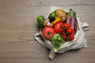 Photo of Bag full of fresh vegetables on wooden background, top view. Space for text
