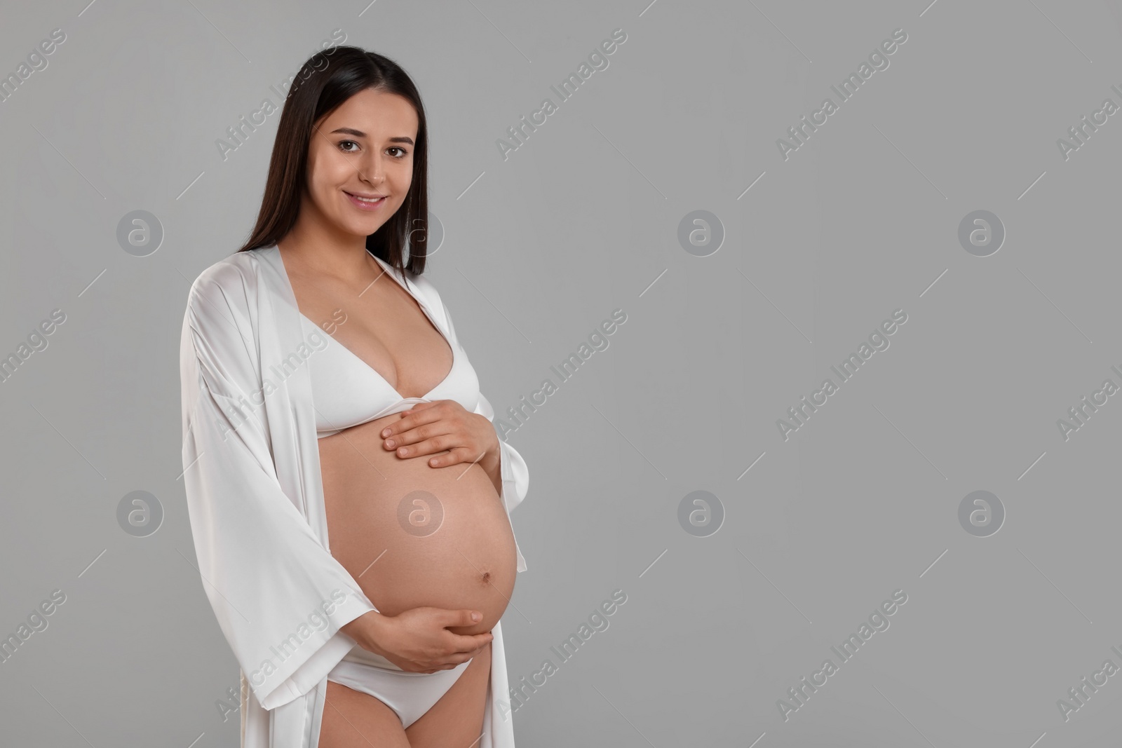 Photo of Beautiful pregnant woman in stylish comfortable underwear and robe on grey background, space for text