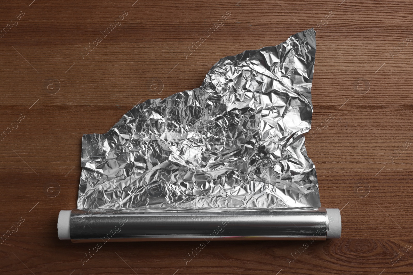 Photo of Roll of aluminum foil on wooden table, top view