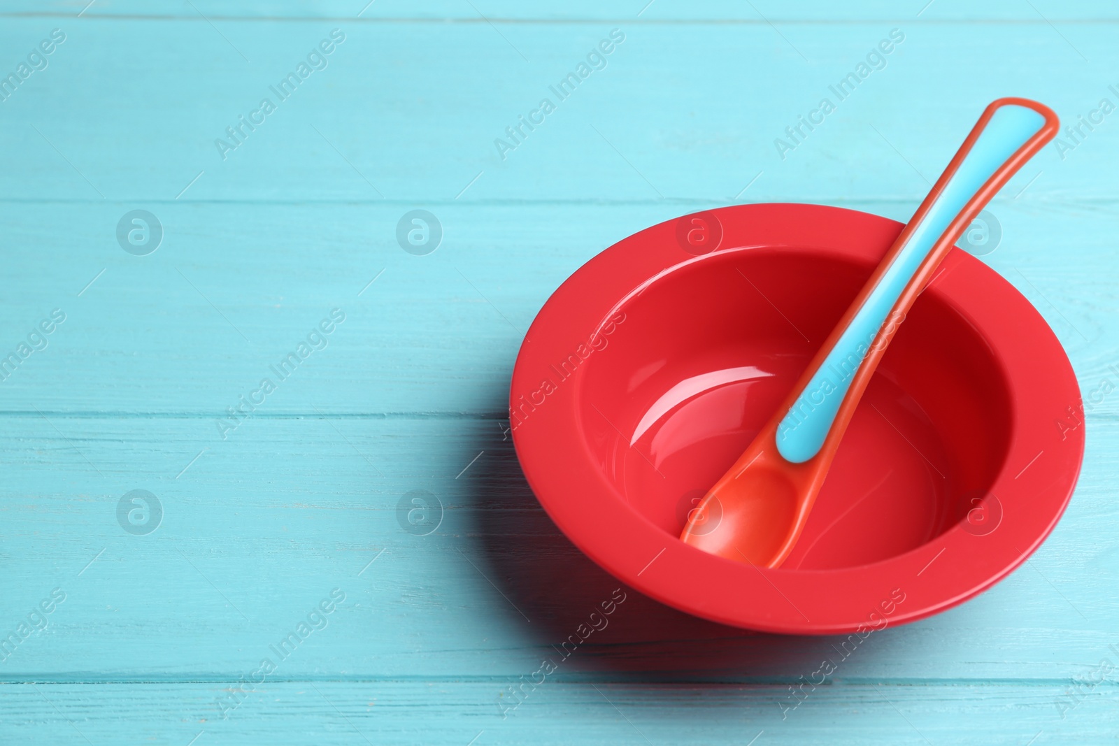 Photo of Plastic plate and spoon on light blue wooden table, space for text. Serving baby food