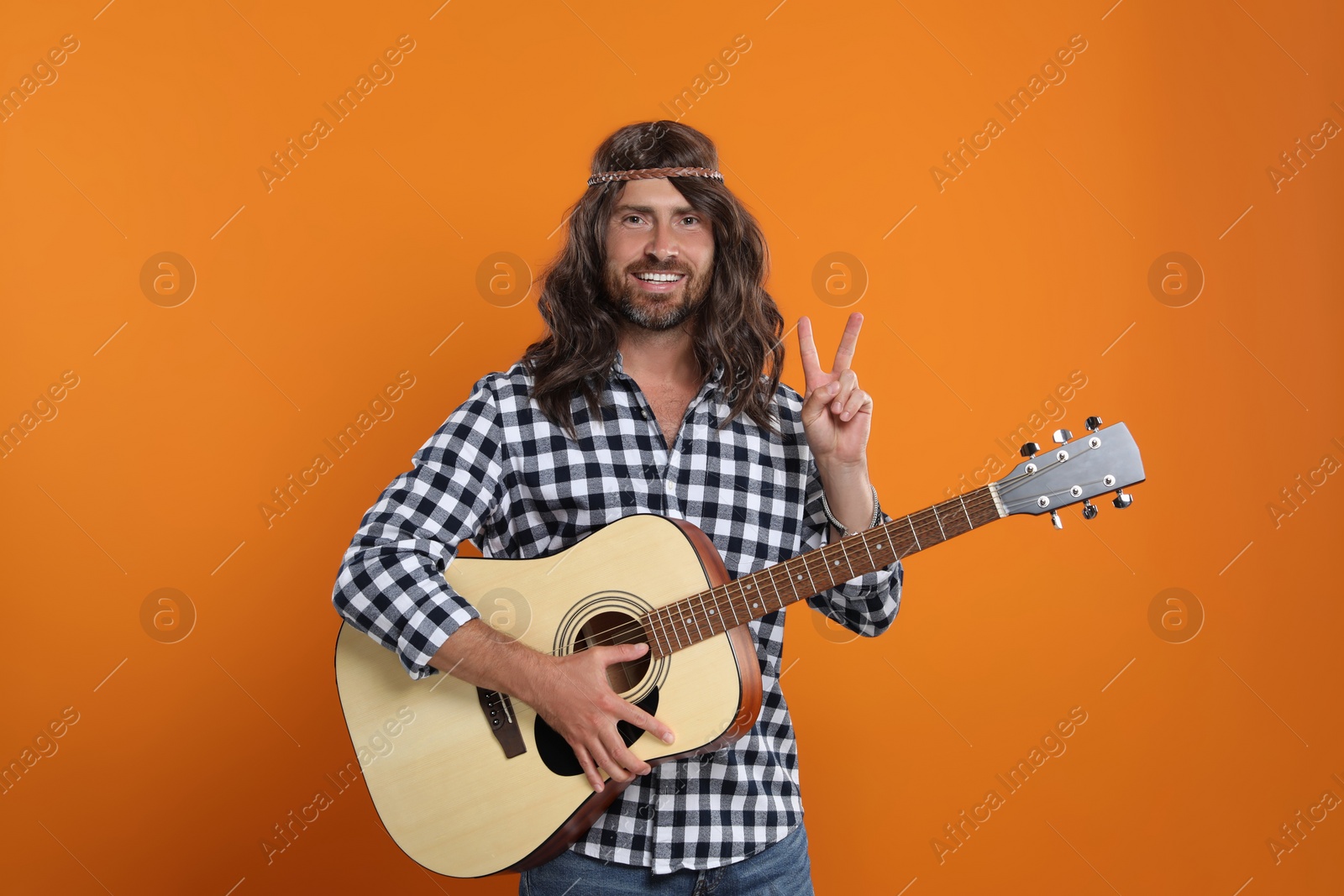 Photo of Hippie man with guitar showing V-sign on orange background