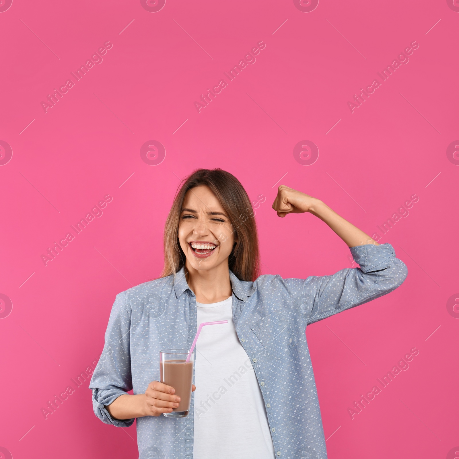 Photo of Young woman with glass of chocolate milk showing her strength on pink background