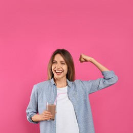 Young woman with glass of chocolate milk showing her strength on pink background