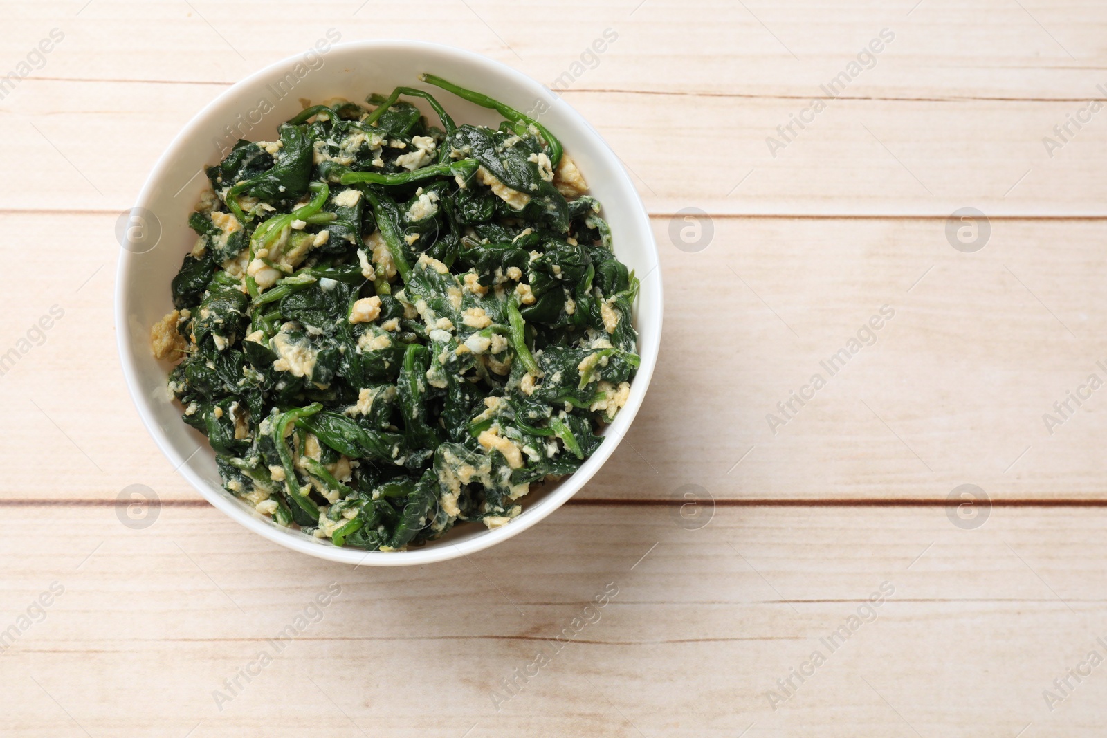 Photo of Tasty spinach dip with eggs in bowl on light wooden table, top view. Space for text