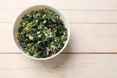 Photo of Tasty spinach dip with eggs in bowl on light wooden table, top view. Space for text