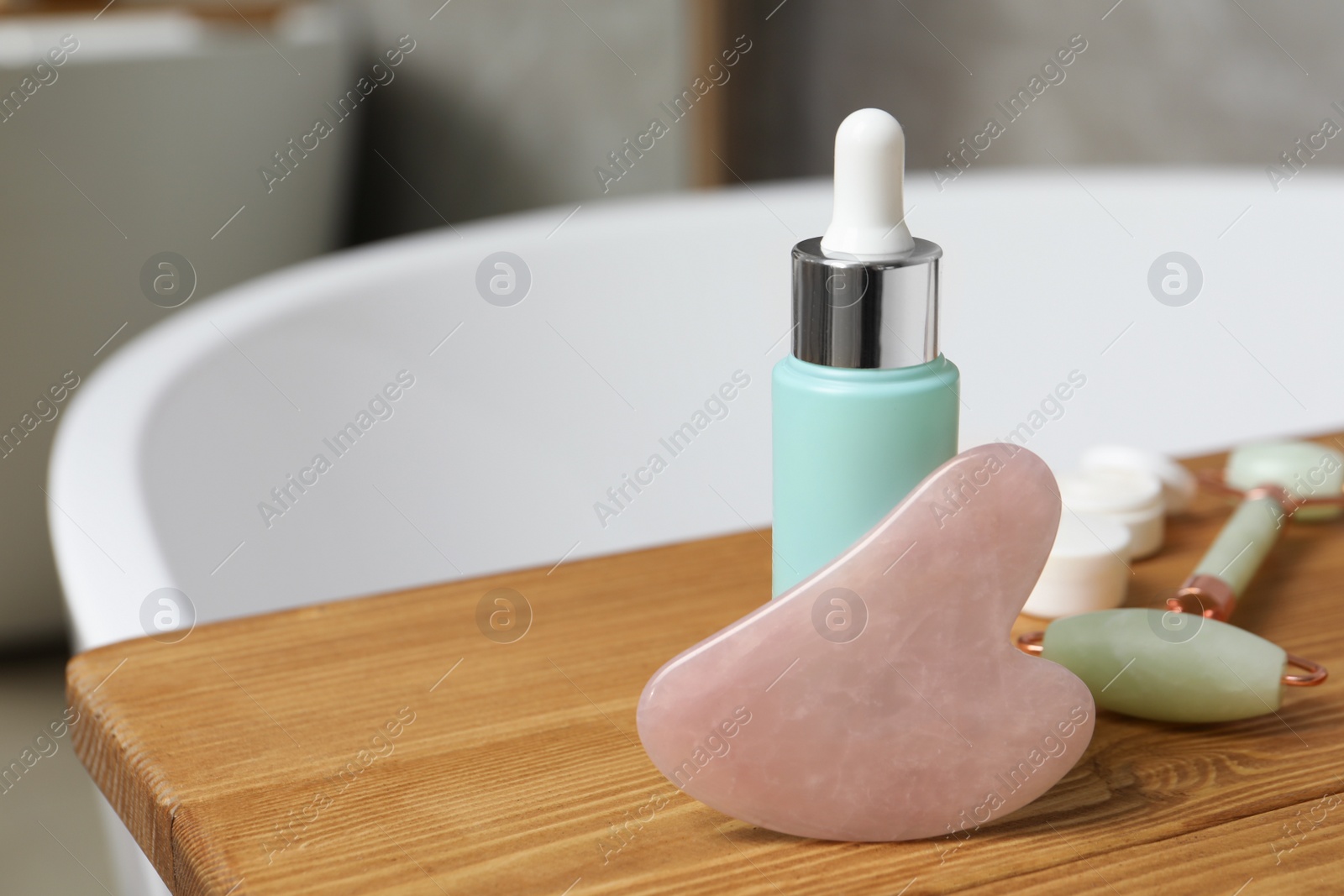 Photo of Rose quartz gua sha tool, natural face roller and cosmetic product on wooden bath caddy. Space for text