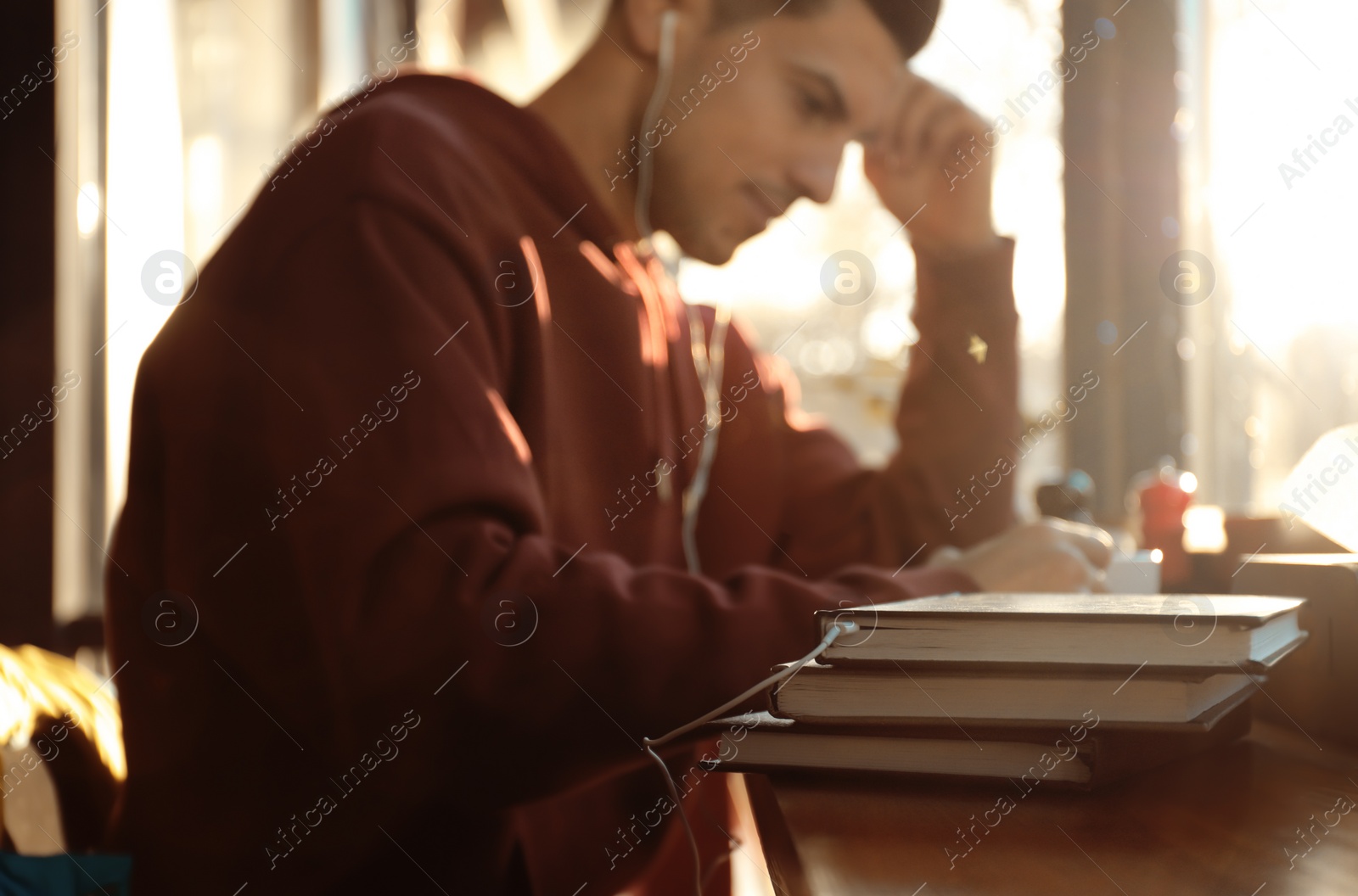 Photo of Man with headphones connected to book at table in cafe