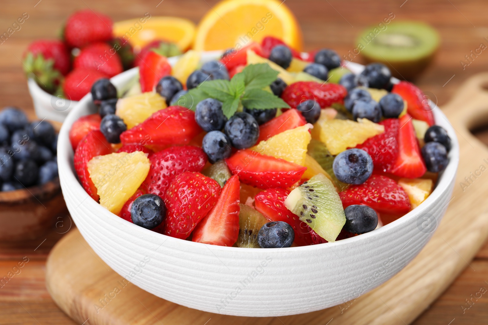 Photo of Delicious fresh fruit salad in bowl on wooden table, closeup